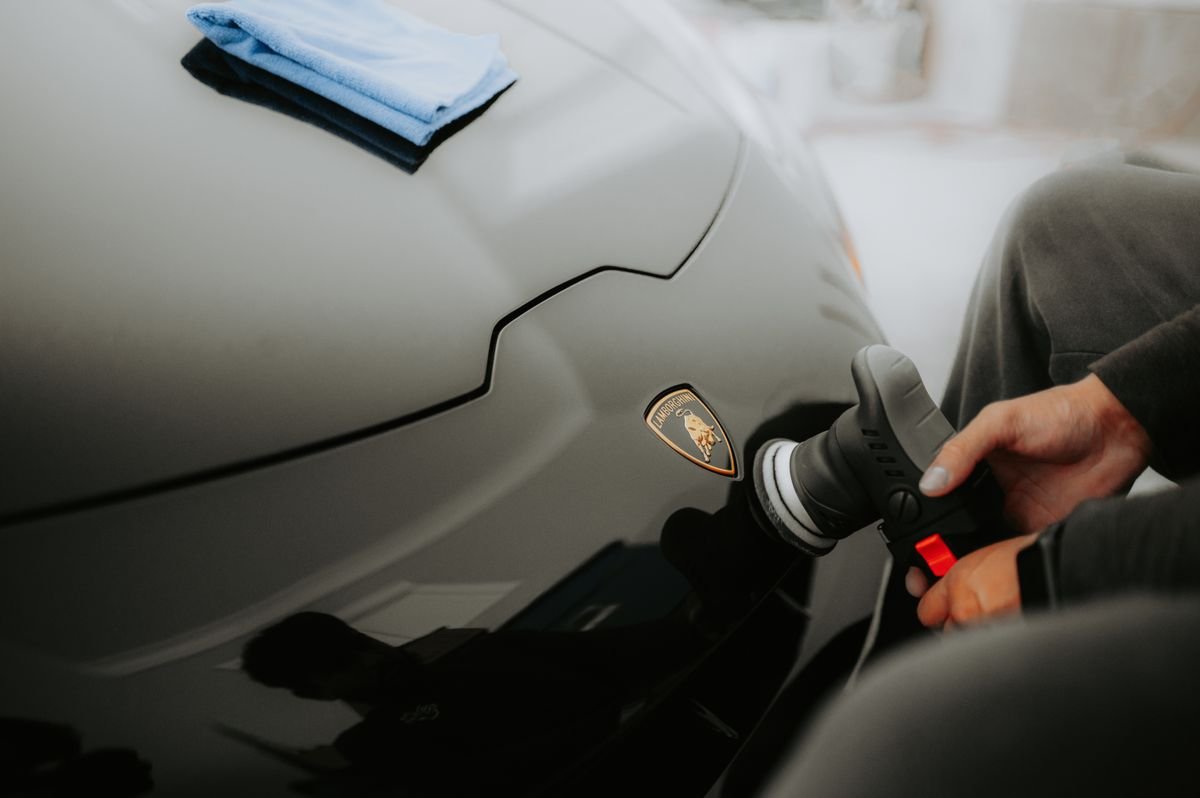 Hand polishing a car exterior with a machine polisher